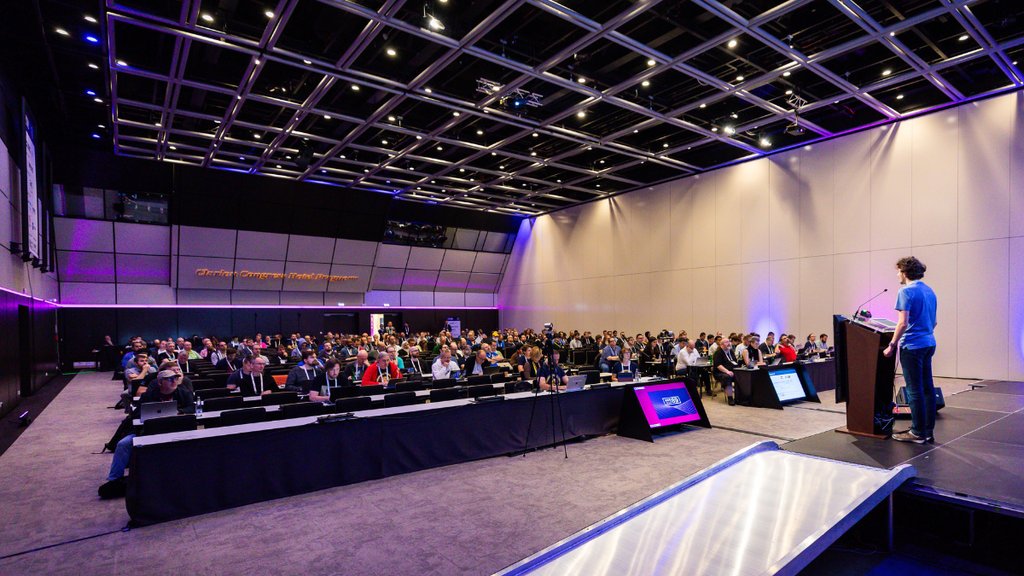 A man on stage presents to a room of people.